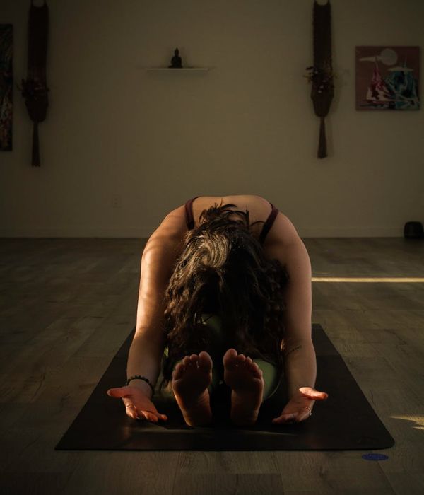 Woman in a calm, focused yoga pose against a dark, warm background.